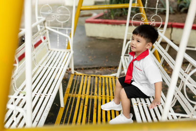 Cute boy playing while sitting on swing outdoors