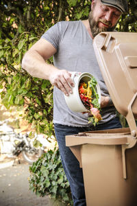 Mature man throwing kitchen scraps into bio-waste container