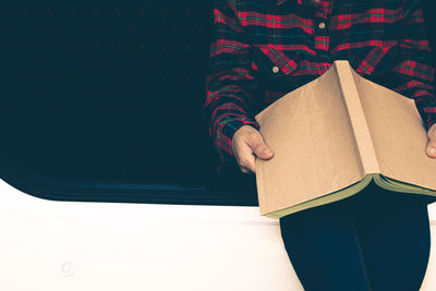 Midsection of person holding book while standing on paper