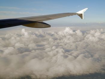 Airplane wing over clouds against sky