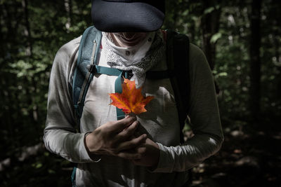 Midsection of man holding orange plant in forest