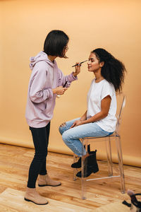 Full length of artist applying make-up on woman face in studio