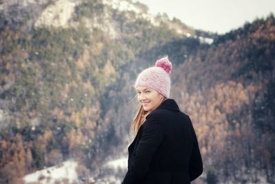 Portrait of smiling woman standing against mountain during winter