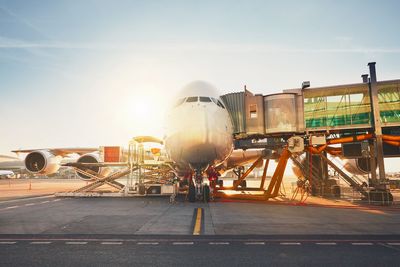 Airplane on airport runway against sky during sunset