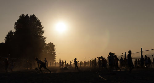 Silhouette people playing volleyball at beach during sunset