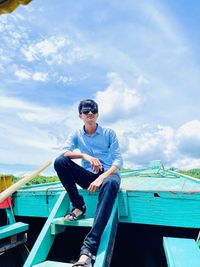 Young man sitting on boat against sky