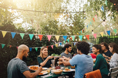 Young male and female friends enjoying dinner during garden party