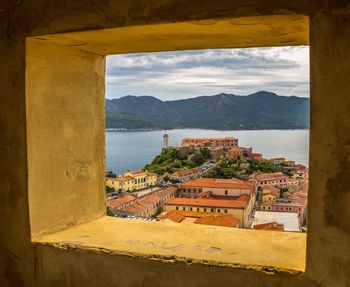 Buildings by sea against sky seen through window