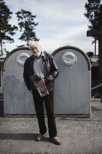 Portrait of senior man standing against recycling bins in city