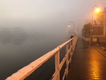 Illuminated street light by lake against sky during foggy weather