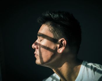 Close-up of eyes closed young man with sunlight on face in darkroom