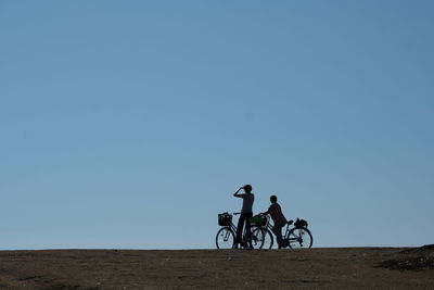 People riding bicycle on desert against clear sky