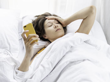 Woman holding mobile phone lying on bed at home