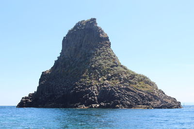 Rock formation by sea against clear sky