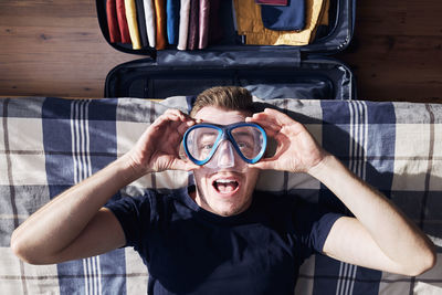 Crazy portrait of happy young man during packing suitcase and planning travel adventure.