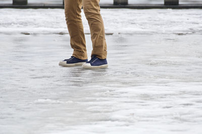 Low section of man standing on shore at beach during winter