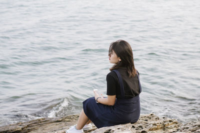 Young woman sitting on shore against sea