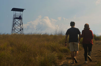 Rear view of couple walking on field against sky