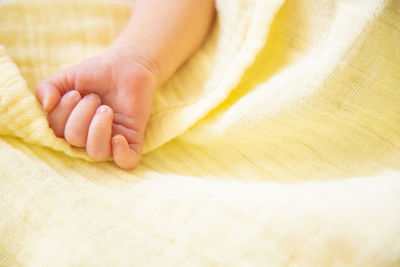 Low section of baby hand on bed, yellow background 