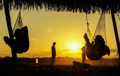 Silhouette men sitting against sky during sunset