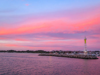 Lighthouse by sea against sky during sunset
