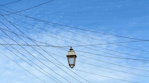 Low angle view of lighting equipment hanging from cable against blue sky