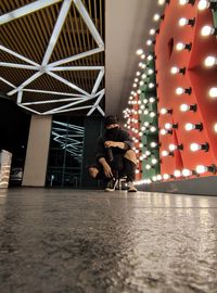 Woman sitting by illuminated lights at ceiling