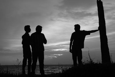 Silhouette people standing by sea against sky during sunset