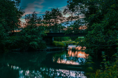 Trees by lake against sky during sunset