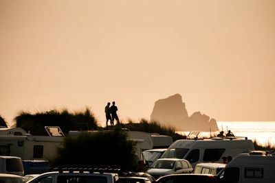 Silhouette people on mountain by sea against sky during sunset