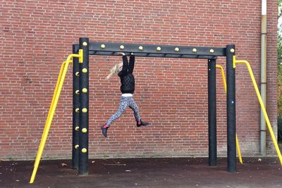 Full length of girl playing with outdoor play equipment against brick wall