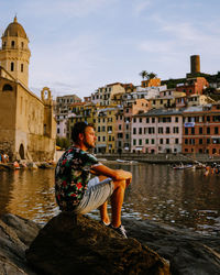 Woman sitting by canal against buildings in city