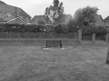 Empty bench in park by building against sky