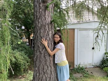 Woman standing by tree trunk against plants, giving a hug to the tree