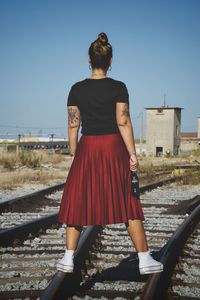 Rear view of woman on railroad tracks against clear sky