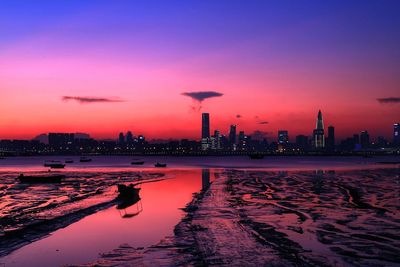 Silhouette buildings by sea against sky during sunset