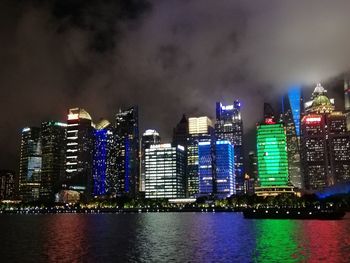 Illuminated buildings by river against sky at night