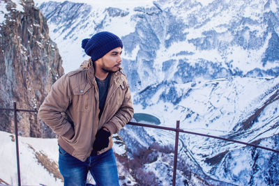 Young man standing against snowcapped mountains