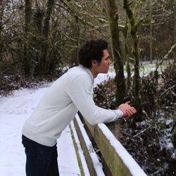 Side view of man leaning on railing at snow covered field