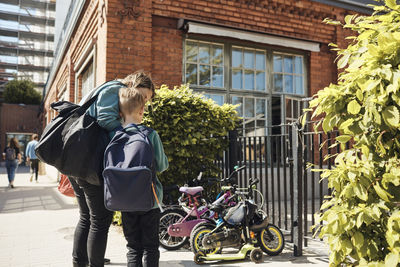 Woman standing with son at school gate on sunny day