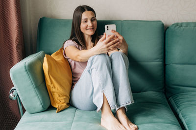 A middle-aged woman sitting on a sofa communicates by video call in a mobile phone.