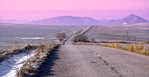 Road by mountains against sky during winter