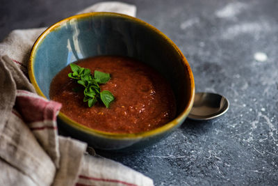 Tomato cream soup with oregano served in a bowl and cutlery on concrete background with copy space
