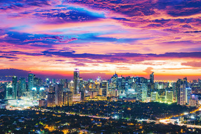 Illuminated buildings in city against sky at sunset