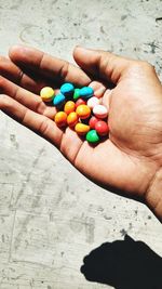 Cropped hand holding multi colored candies over footpath