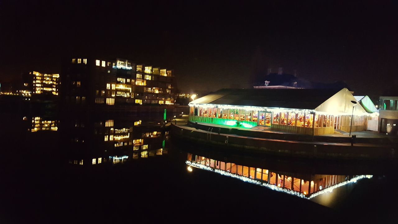 ILLUMINATED CITYSCAPE BY RIVER AGAINST SKY