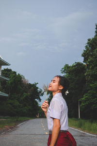 Side view of girl standing by tree against sky