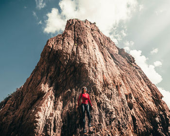 Low angle view of person standing on rock against sky