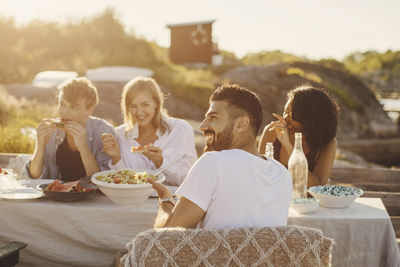 Happy friends enjoying lunch at table on jetty