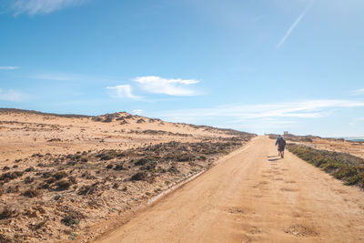Rear view of man walking on dirt road against sky